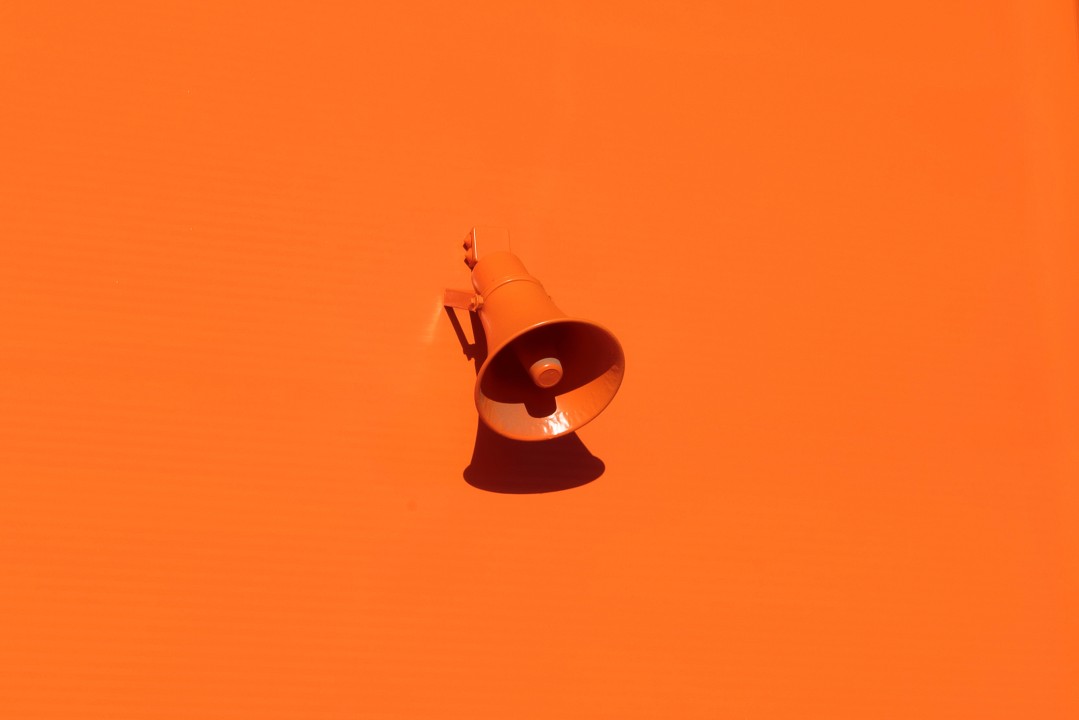 Megafone laranja preso a uma parede laranja